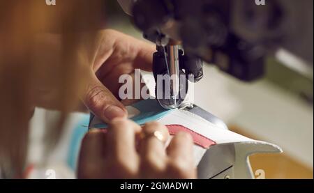 Factory worker making details for new leather shoes on industrial sewing machine Stock Photo