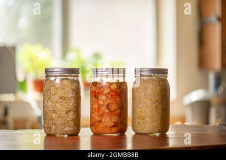 Three mason jars with kimchi and sauerkraut on kitchen counter Stock Photo
