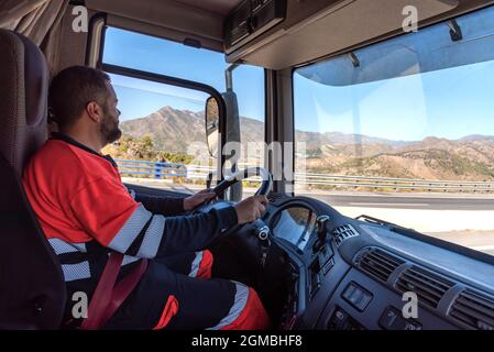 Truck driver in the driving position with both hands holding the steering wheel and driving. Stock Photo