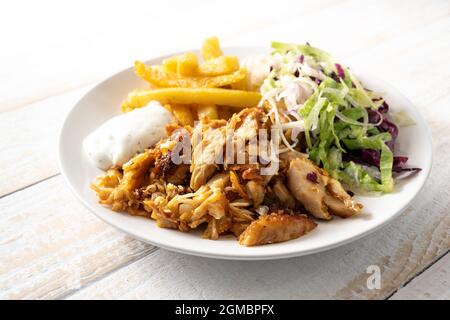 Roasted chicken meat from a doner kebab with french fries, salad and tzatziki dip on a plate and on a wooden table, copy space, selected focus, narrow Stock Photo