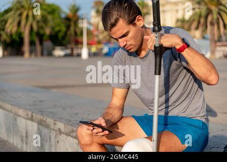 Young latin man with crutches using mobile phone after doing exercise Stock Photo