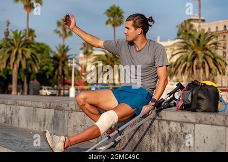 Young latin man with crutches taking a selfie after doing exercise Stock Photo