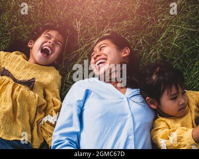 Happy mother and daughters smiling and laughing lying on the lawn in summer park. Family spend their free time together on vacation. Stock Photo