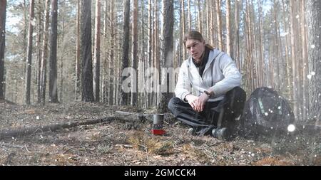 A man in a campaign drinks tea. A young traveler in the forest camped and cooked breakfast in nature. The naturalist drinks hot fresh tea cooked on op Stock Photo