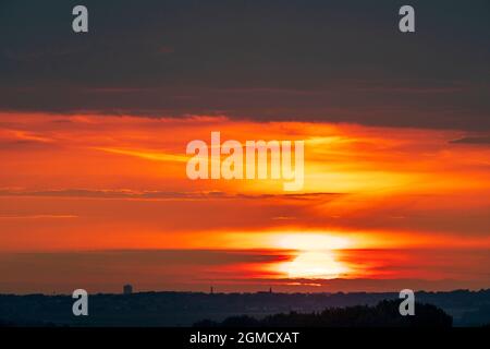 Sunrise over the distant Kent town of Margate seen from the village of Reculver. Sun rising into a narrow band of vivid red sky with some clouds and above thick dark rain clouds filling the sky. Stock Photo