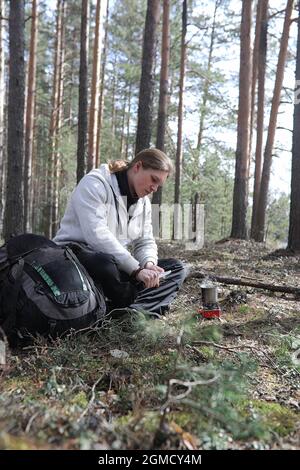 A man in a campaign drinks tea. A young traveler in the woods camped and cooked breakfast in nature. The naturalist drinks hot fresh tea cooked on ope Stock Photo