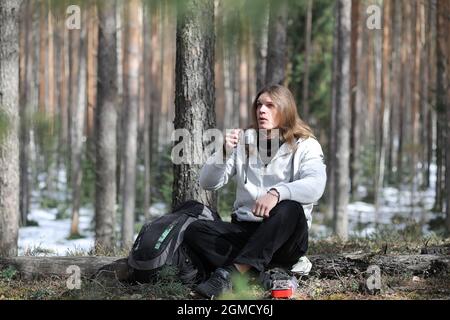 A man in a campaign drinks tea. A young traveler in the woods camped and cooked breakfast in nature. The naturalist drinks hot fresh tea cooked on ope Stock Photo