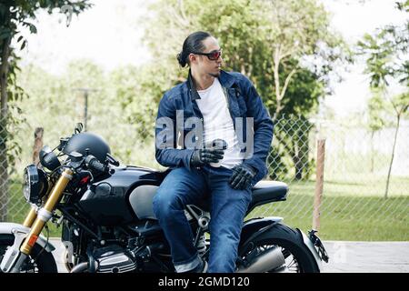 Handsome stylish man sitting on motorcycle with cup of take out coffee and looking away Stock Photo