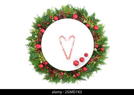 Christmas table setting with plate, candy canes and red baubles with holly and winter greenery on white background. Stock Photo