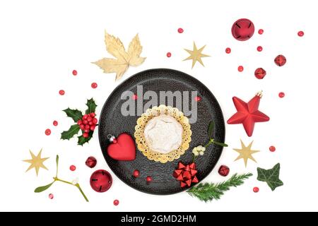 Christmas mince pie on a plate with winter greenery, loose holly berries, gold leaves, stars and bauble tree decorations. Stock Photo