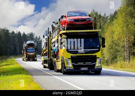 Two vehicle carriers, yellow Volvo FM truck in the front, haul new cars on road 52 from Hanko Port to mainland. Raasepori, Finland. September 9, 2021. Stock Photo