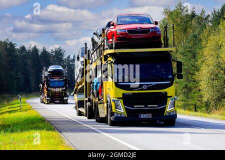 Two vehicle carriers, yellow Volvo FM truck in the front, haul new cars on road 52 from Hanko Port to mainland. Raasepori, Finland. September 9, 2021. Stock Photo