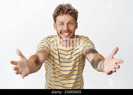 Handsome blond man reach hands to hold someone, stretching out arms for hug, waiting for big cuddle, standing over white background Stock Photo