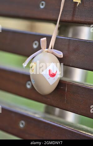 Closeup view of light beige plastic decorative Easter egg tied with ribbon on dark brown bench at university campus, Belfield, Dublin Ireland Stock Photo