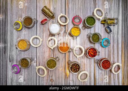 Open spice jars viewed from top view showing cinnamon, sesame, curry, cayenne, oregano, peppercorns, dried bay leaves, turmeric, on wooden table Stock Photo