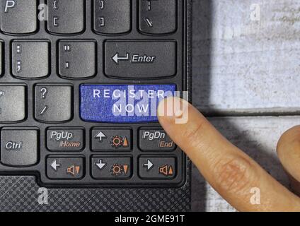 Finger pressing a blue key labeled REGISTER NOW with symbol on a computer keyboard concept Stock Photo
