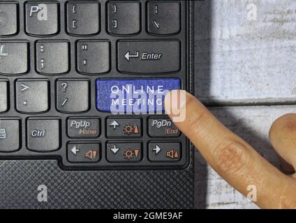 Finger pressing a blue key labeled ONLINE MEETING with symbol on a computer keyboard concept Stock Photo