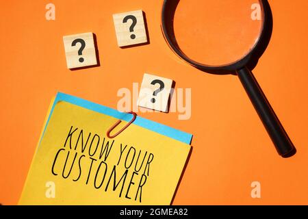 KNOW YOUR CUSTOMER text on color notepaper, wooden cube with question mark and magnifying glass on orange background. Stock Photo