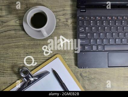 Business, Question and Answer concept. Top view of Q and A text, coffee, pen, laptop and paper clipboard on wooden table. Stock Photo