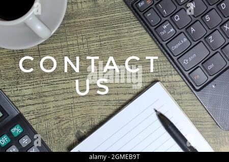 CONTACT US text surrounded by laptop, coffee, pen and paper. Stock Photo