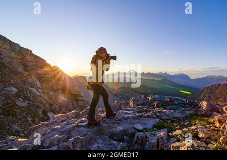 Woman photographer takes photos on the mountain top. Outdoor activity, hiking, active vacation and wanderlust concept. Stock Photo