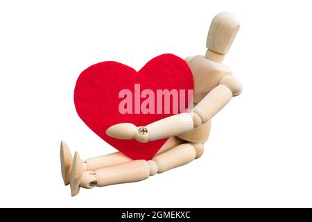 Wooden dummy hug a heart shape that made from acrylic felt fabric. Wooden puppet sitting isolated on white background. Valentine's day concept Stock Photo