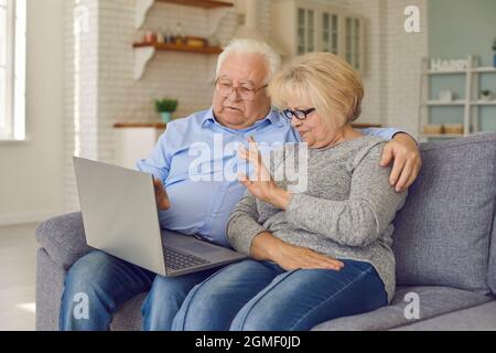 Aged senior couple waving hands greeting grandchildren through facetime using laptop. Stock Photo