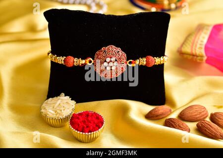 Rakhi with roli chawal and almonds on yellow silk background Stock Photo