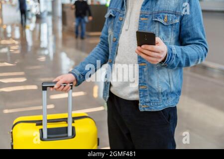 Man using mobile phone at airport. Urban traveler wearing casual holds smartphone, guy texting message while holding suitcase luggage in airport Stock Photo