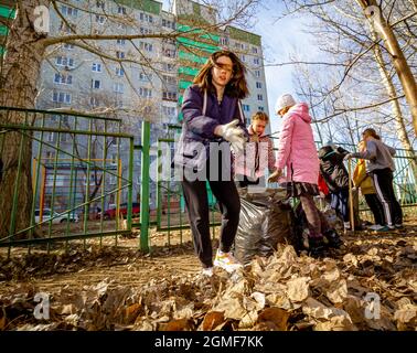 Omsk, Russia. 24 April, 2021. A schoolgirl in a dark jacket with her hands gathered the fallen leaves. Traditional Russian events for the preparation Stock Photo