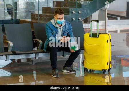 Man using mobile phone at airport lobby . Urban traveler wearing casual holds smartphone, guy texting message while holding suitcase luggage in Stock Photo