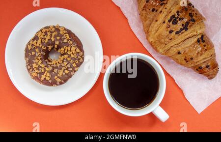 One chocolate donut, croissant and black Americano coffee without milk in a white cup on a bright background. Top view, flat lay. Freshly brewed or Stock Photo
