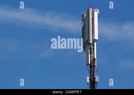 Mobile cell phone tower against the background of a blue sky and white cloud. Telecommunication TV tower. Cellular antenna. Wi-fi transmitter Stock Photo