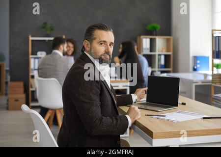 Portrait of senior business executive sitting at desk with laptop in modern office Stock Photo