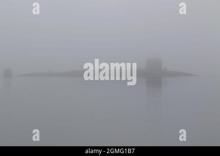 The eerie silhouette of the Trident-armed HMS Vigilant (S30), a Vanguard-class submarine operated by the Royal Navy, passing a fog-bound Gourock on the Firth of Clyde, Scotland. Stock Photo