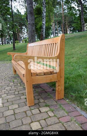 An empty figured wooden bench in profile stands in a summer park on a stone paving slab Stock Photo