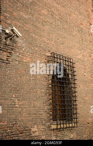 On an old brick wall hangs a wrought iron grate on the window. A video camera for outdoor security surveillance is attached above the window. Stock Photo