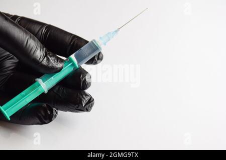 Hand in a black glove with a plastic syringe and a needle on a white background Stock Photo