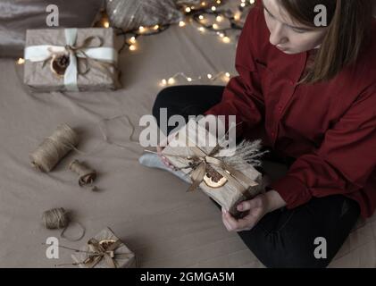 Girl with a Christmas gift, decorated with dried flowers and a dry orange, wrapped in craft paper. Stock Photo