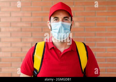 Portrait of delivery man in red uniform and thermal backpack standing outdoors Stock Photo