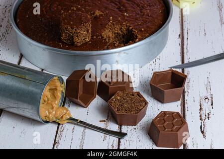 Small Brazilian honey cake, next to a can of dulce de leche and small forms of chocolate. In the background a cake on a baking sheet. Stock Photo