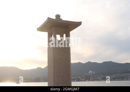 Stone lantern on Miyajima island, Hiroshima, Japan. Land in the background of stone lantern is Hiroshima. Stock Photo