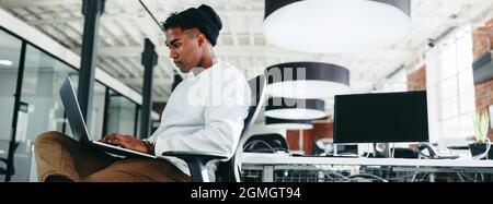 Computer programmer working on a new code in an office. Focused young businessman using a laptop while sitting in a modern workplace. Creative busines Stock Photo