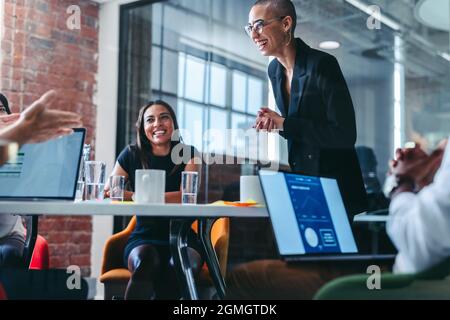 Young businesswoman receiving praise from her colleagues during a meeting in a modern office. Successful young businesswoman smiling cheerfully while Stock Photo
