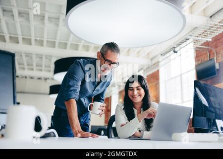 Creative businesspeople making success in the office. Happy mature businessman collaborating with his female colleague in a modern workplace. Two coll Stock Photo