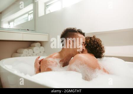Lovely queer couple enjoying a romantic bubble bath together. Happy young couple having fun together in the bathtub. Young LGBTQ+ couple spending qual