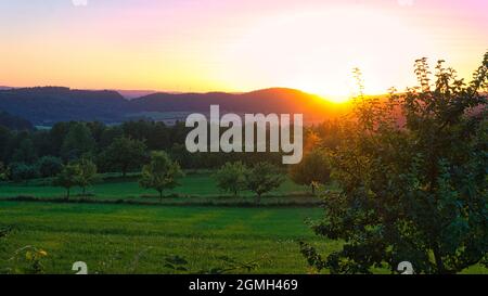 Sunset in Saarland on a meadow with trees and view into the valley. a warm light mood in orange, red and gold Stock Photo