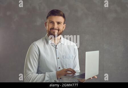 Confident smiling business expert man holding laptop standing on studio wall Stock Photo