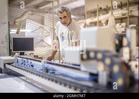 Factory worker technician works on large CNC digital cutter machine for cutting fabric textile material Stock Photo