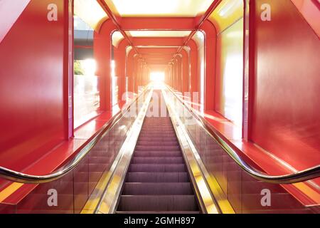 A low angle view of a pure red long escalator with sunshine at the top Stock Photo